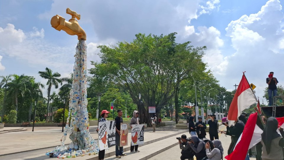 Sejumlah aktivis lingkungan berunjuk rasa dengan membawa kran raksasa berisi sampah yang mengalir di depan alun-alun Sidoarjo, Senin (19/5/2025) (Foto : Eleanor/tagarjatim.id)